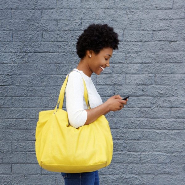 Side portrait of a happy young woman with a bag reading text message on her mobile phone