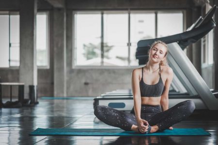 Happy young caucasian woman stretching on yoga mat before working out in fitness gym